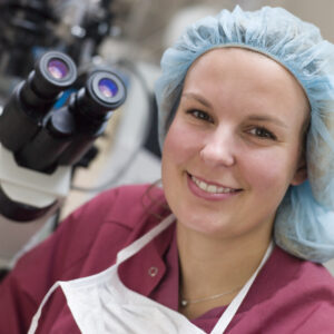 Embryologist sitting by microscope smiling after ICSI | Arizona Reproductive Medicine Specialists