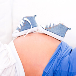Photo of woman's pregnant belly with baby shoes resting on top